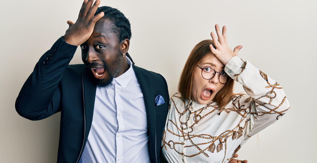 A couple in business attire reacting in shock, both with hands on their foreheads.